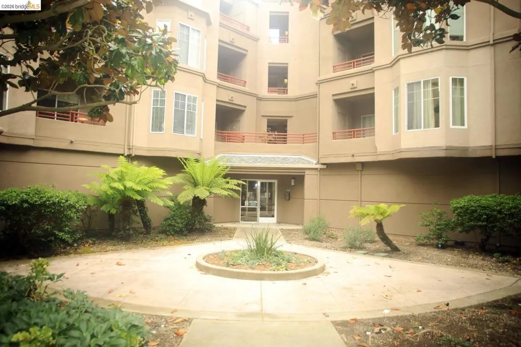 Multi-story building featuring bay windows, individual balconies with red railings, and a central entrance