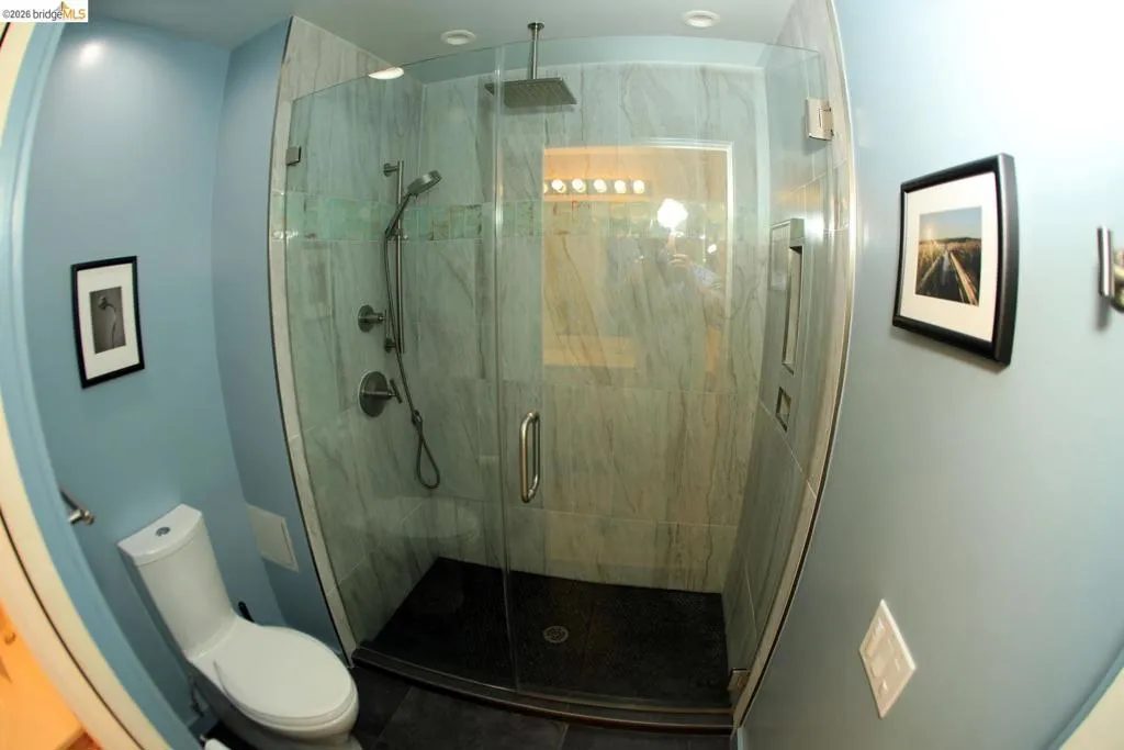 Glass-enclosed shower with a dark base and light-colored tile walls, featuring a rainfall showerhead and handheld sprayer