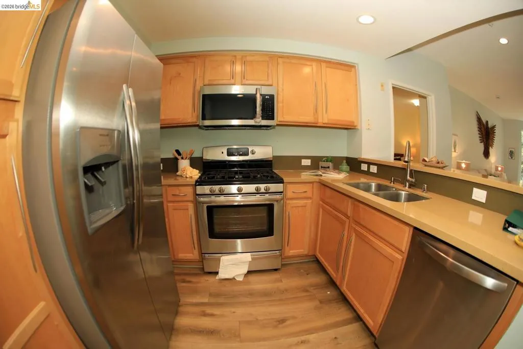 Kitchen featuring stainless steel appliances, wood-finish flooring, light wood cabinetry, a double basin sink, and ample counter space