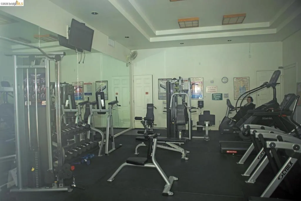 Fitness center featuring comprehensive exercise equipment, mirrored wall panels, recessed lighting, and durable rubber flooring