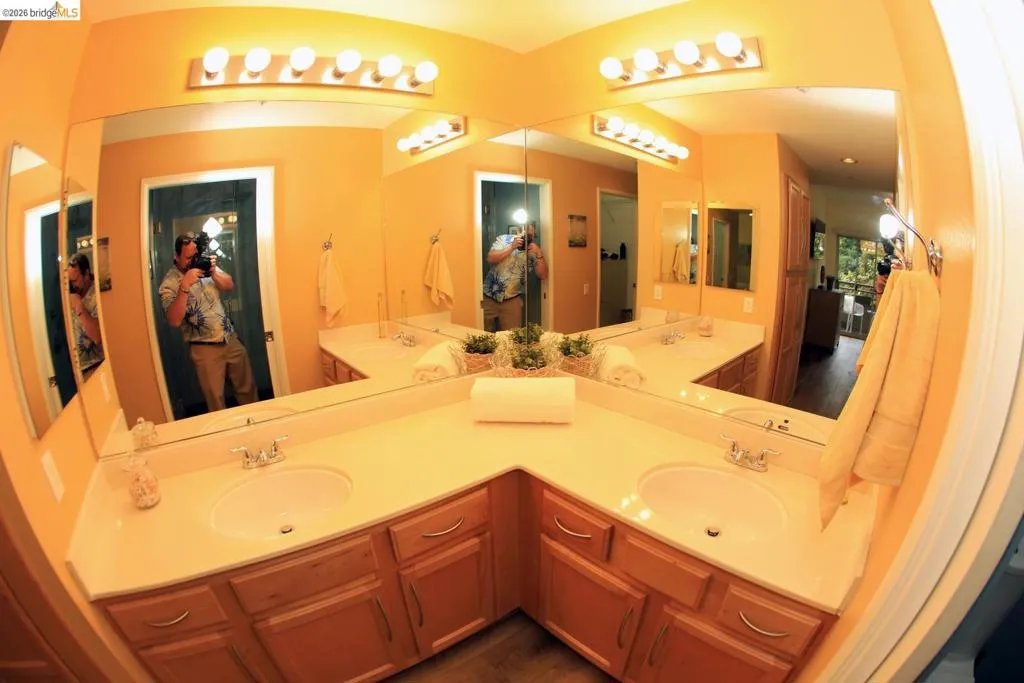 Corner vanity featuring dual undermount sinks, light-toned countertops, and wood-finish cabinetry