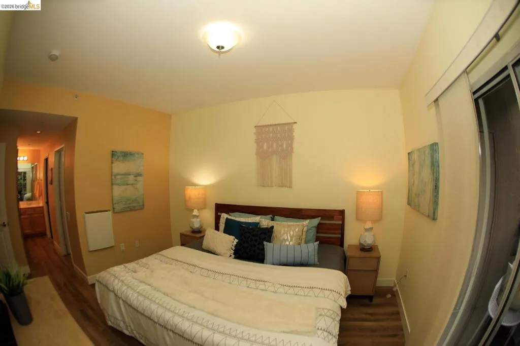 Bedroom featuring wood-finish flooring, a contemporary ceiling light fixture, and a sliding glass door with a roller shade