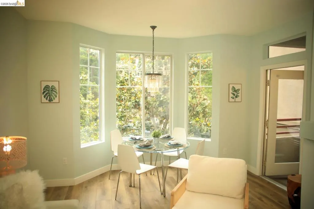 Bay window dining area featuring multiple windows, wood-finish flooring, and a chandelier-style light fixture