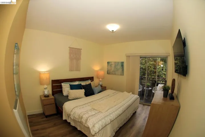 Bedroom featuring wood-finish flooring, a ceiling-mounted light fixture, and a sliding glass door providing access to an exterior balcony
