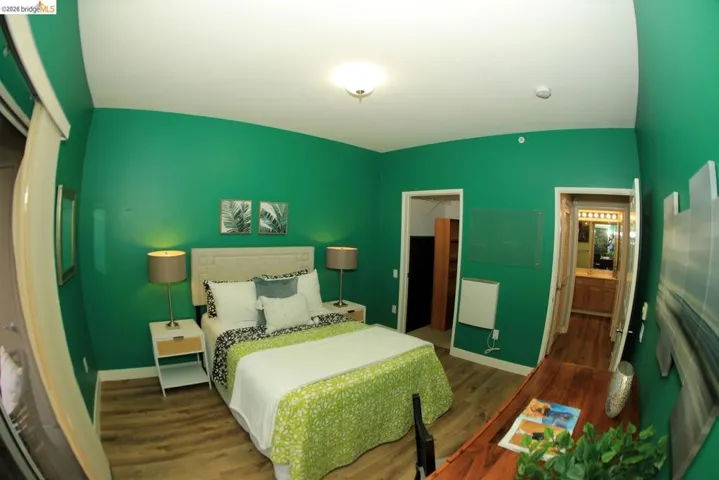 Bedroom featuring wood-finish flooring, a neutral upholstered headboard, and a built-in wall heater