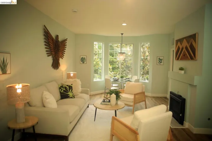 Open-concept living area featuring wood-finish flooring, a contemporary fireplace with mantel, and a bay window with multiple vertical panes