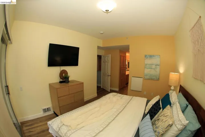 Bedroom featuring wood-finish flooring, a wall-mounted television, and a built-in light fixture