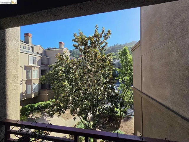 Exterior balcony with metal railing, featuring mature trees and distant residential architecture