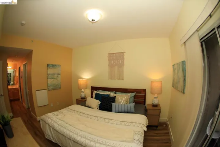 Bedroom featuring wood-finish flooring, a contemporary ceiling light fixture, and a sliding glass door with a roller shade