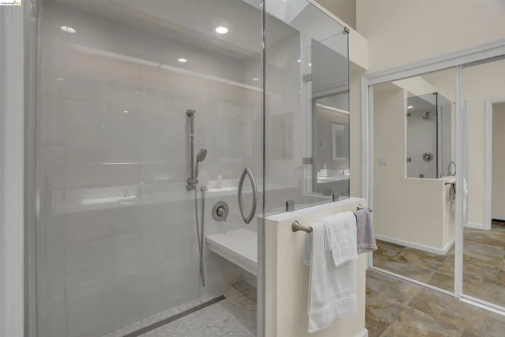 Glass-enclosed shower featuring a handheld showerhead, built-in bench, linear drain, and recessed lighting