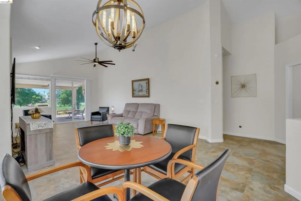 Open-concept living area featuring vaulted ceilings, a contemporary ceiling fan, and large sliding glass doors leading to a patio