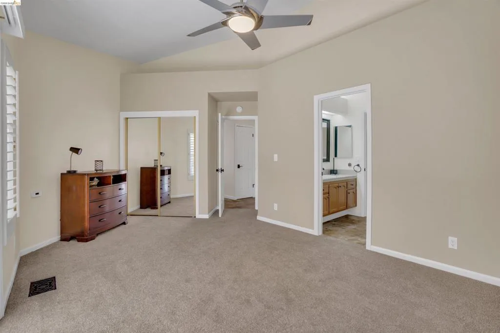 Carpeted room featuring a vaulted ceiling with a flush-mount ceiling fan