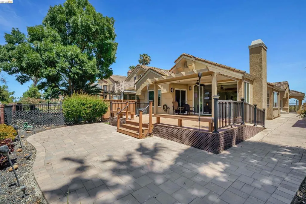 Spacious outdoor living area featuring an expansive paver patio, a raised wood deck with pergola, and a stucco exterior with a prominent chimney