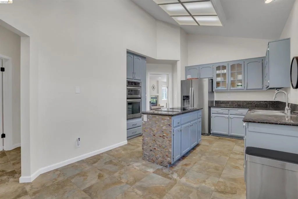 Kitchen featuring light blue cabinetry, built-in stainless steel appliances, dark countertops, and a central island with a mosaic tile facade