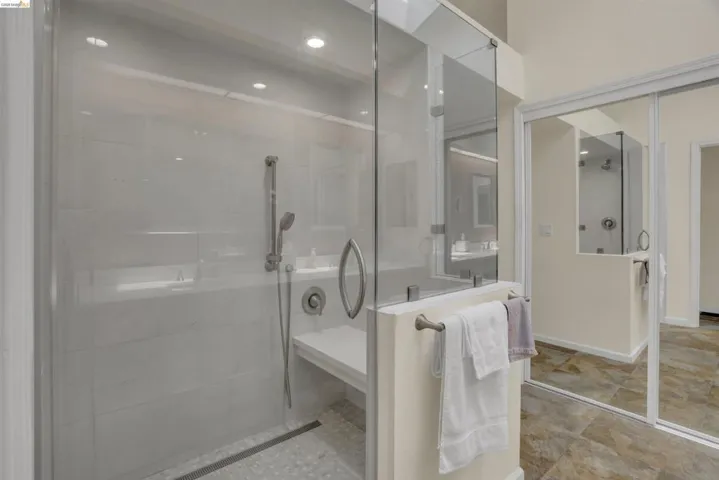 Glass-enclosed shower featuring a handheld showerhead, built-in bench, linear drain, and recessed lighting