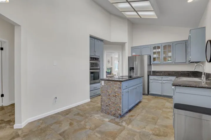 Kitchen featuring light blue cabinetry, built-in stainless steel appliances, dark countertops, and a central island with a mosaic tile facade