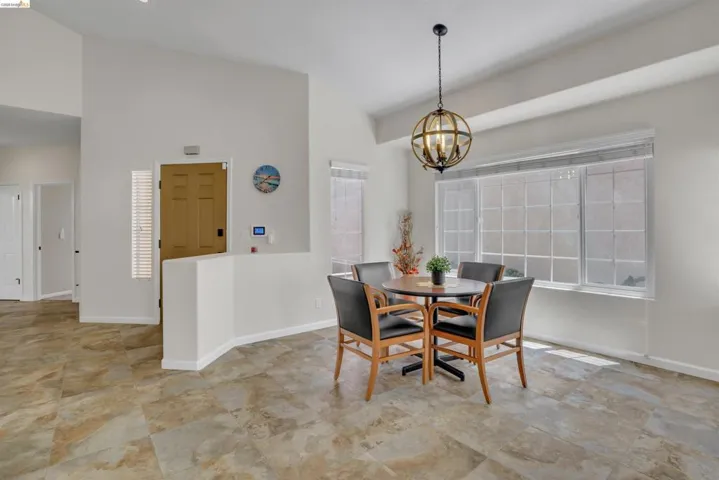 Spacious dining area featuring a prominent multi-pane window, vaulted ceilings, and large-format tile flooring