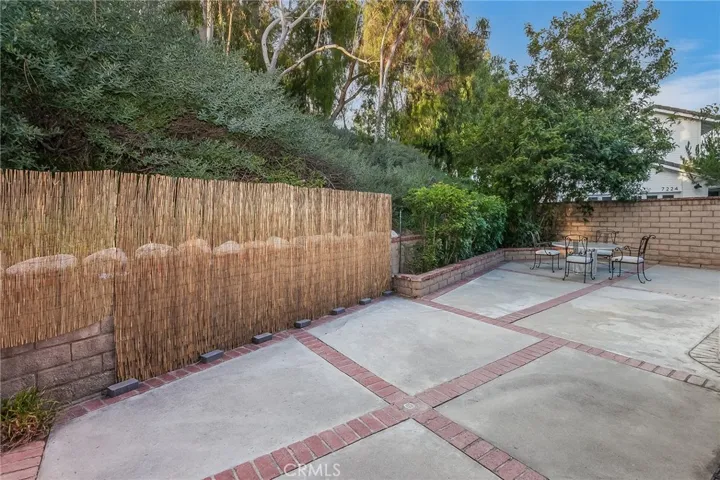 Private backyard with tall Cypress trees, raised flowerbeds, lush greenery, brick and concrete patio space, and natural gas hookup for a future BBQ setup