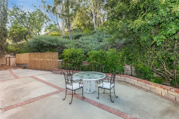 Private backyard with tall Cypress trees, raised flowerbeds, lush greenery, brick and concrete patio space, and natural gas hookup for a future BBQ setup