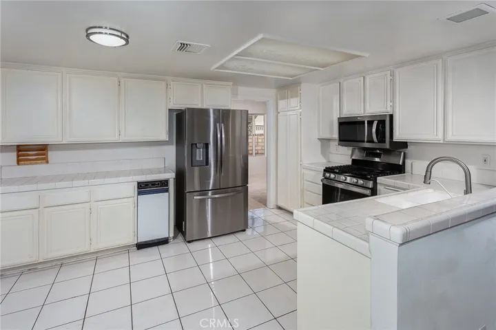 The kitchen opens naturally to the family room and sunny breakfast nook, creating a comfortable everyday gathering space. Features include tile floors and counters, stainless steel appliances, GE® 5-burner gas range, Bosch® silent dishwasher, Whirlpool® microwave, Samsung® refrigerator/freezer, pantry storage, trash compactor, and dual basin sink.