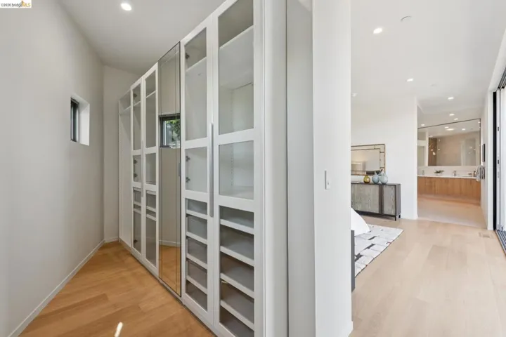 Walk-through closet with extensive built-in cabinetry, glass panel doors, integrated shelving, and wood-finish flooring