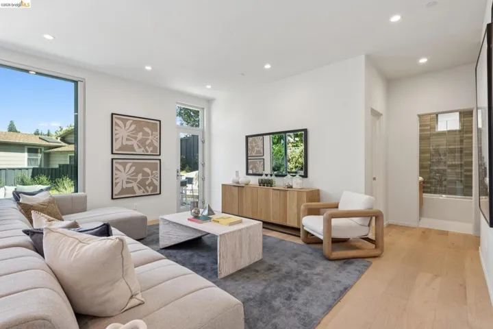 Open-concept living area with large format windows, wood-finish flooring, recessed lighting, and a glass-paneled door