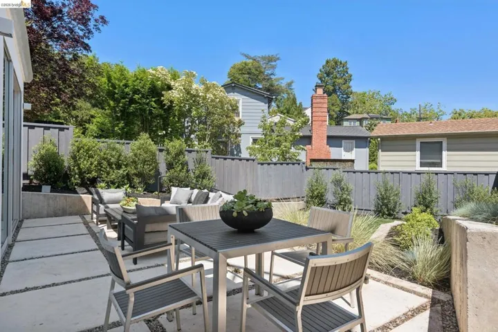 Paved patio featuring large square concrete pavers with gravel accents, surrounded by a dark gray wooden privacy fence and tiered landscaping