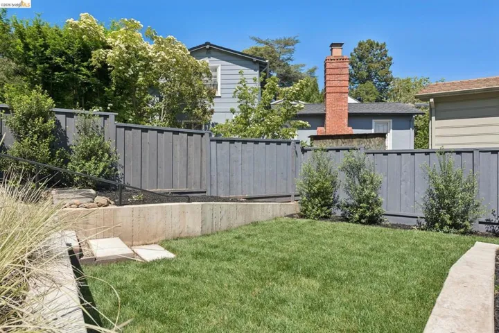 Tiered backyard with a manicured lawn, concrete retaining walls, and a new privacy fence