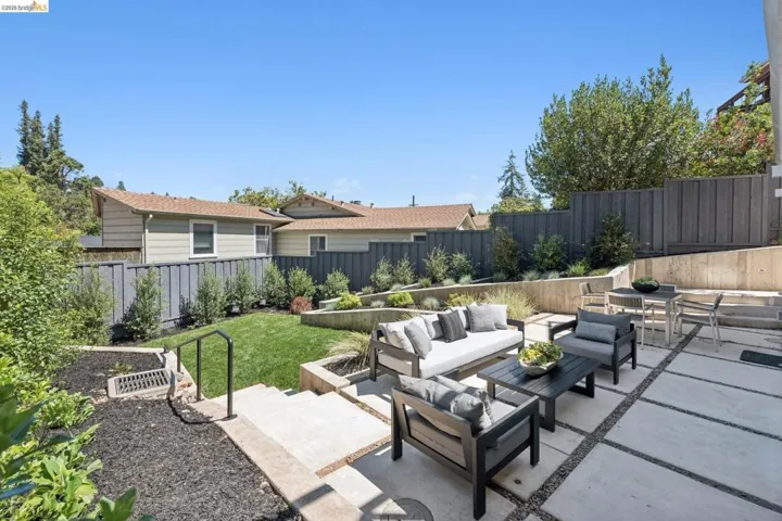 Expansive patio featuring large format concrete pavers, a terraced landscape design, a manicured lawn, concrete retaining walls, and surrounding privacy fencing