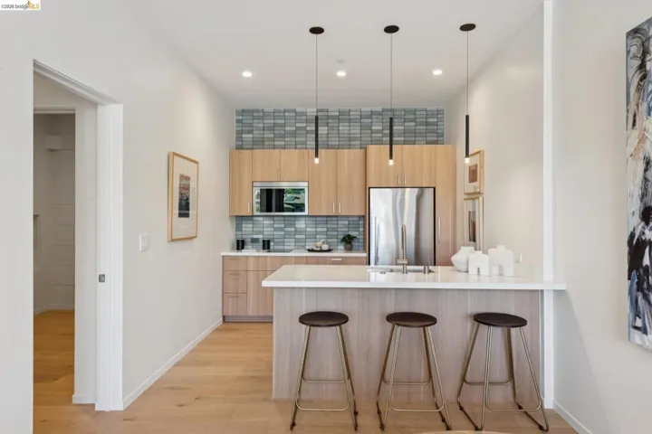 Modern kitchen featuring wood-finish cabinetry, stainless steel appliances, a tile backsplash, and a breakfast bar with a solid surface countertop