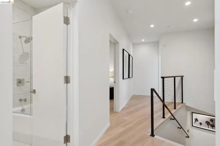 Hallway with light wood-finish flooring, recessed lighting, and a modern metal and cable railing