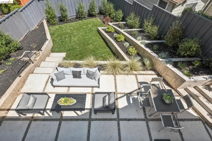 Terraced backyard featuring concrete patio pavers, a manicured lawn, and multi-level planters with established plantings