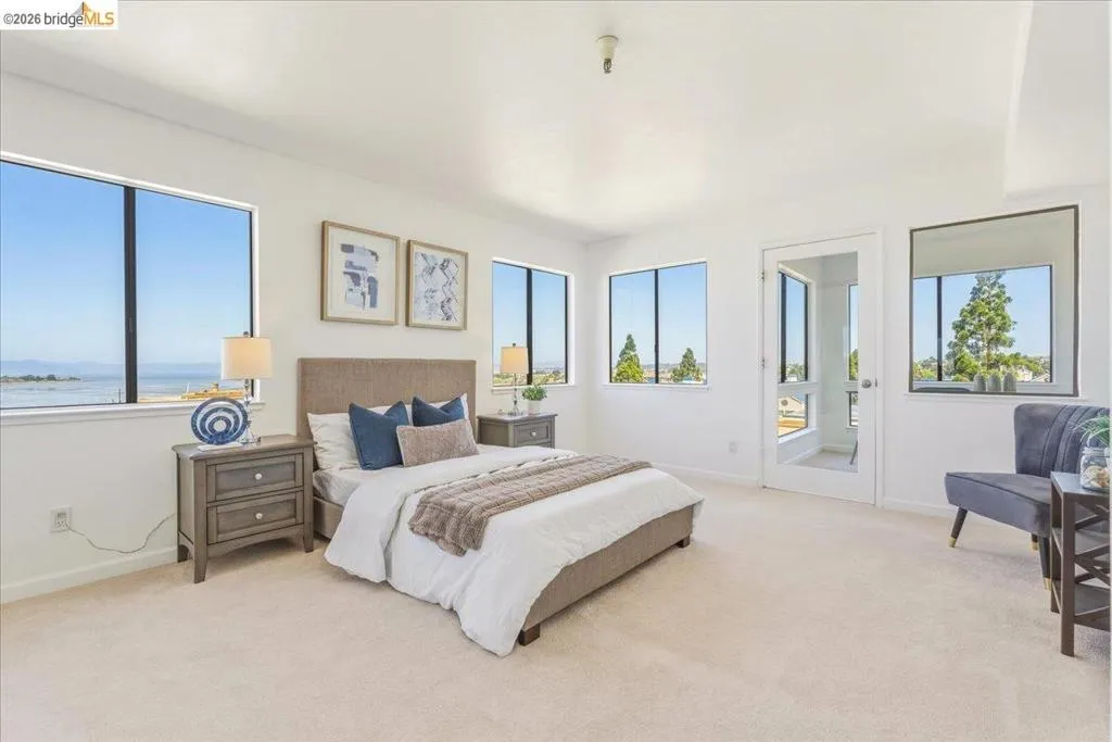 Bedroom featuring multiple windows, light-colored carpeting, white walls, and a glass-paneled door Bedroom featuring multiple windows, light-colored carpeting, white walls, and a glass-paneled door