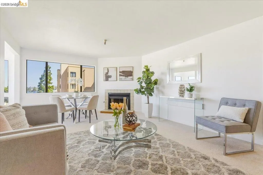 Living area featuring a fireplace with a light tile surround, large windows, and neutral carpeting Living area featuring a fireplace with a light tile surround, large windows, and neutral carpeting
