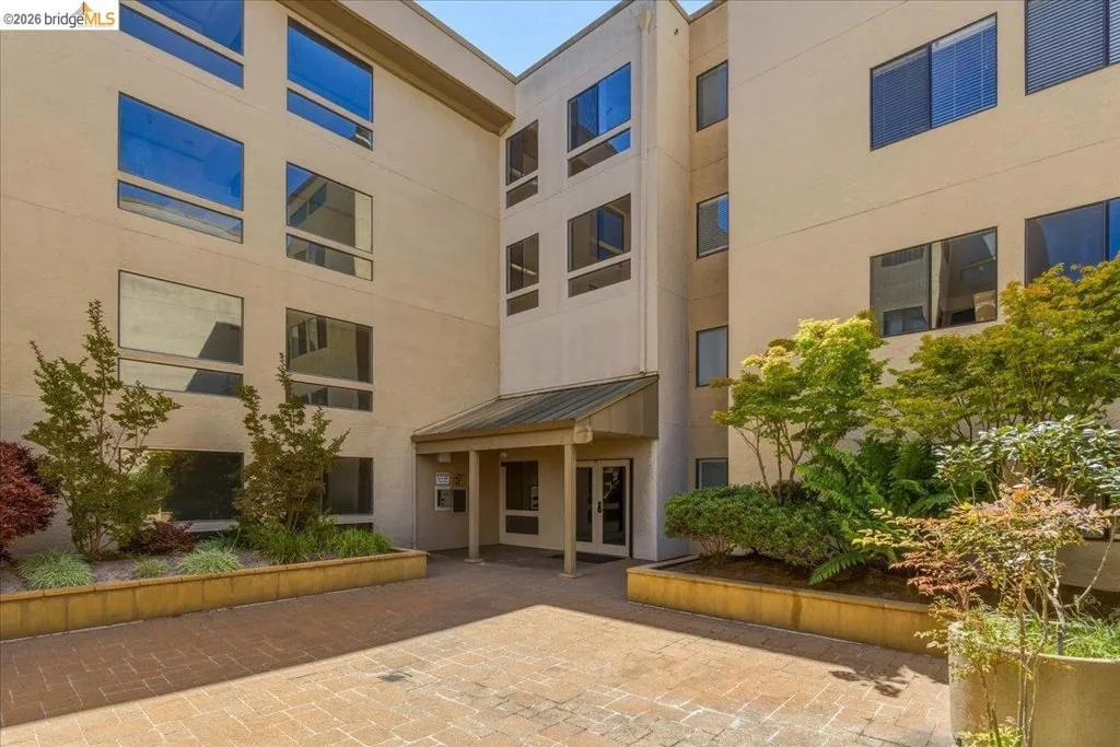 Multi-story building exterior featuring a covered entryway, brick paver courtyard, and integrated landscaping with mature plantings Multi-story building exterior featuring a covered entryway, brick paver courtyard, and integrated landscaping with mature plantings