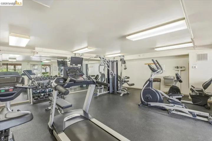Fitness center featuring mirrored walls, multiple cardio machines, weight training equipment, and resilient rubber flooring