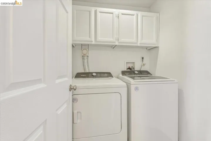 Dedicated laundry space featuring white paneled upper cabinetry, white walls, and a white interior door