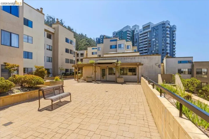 Expansive paver patio bordered by raised planters and mature shrubbery, offering an open communal area