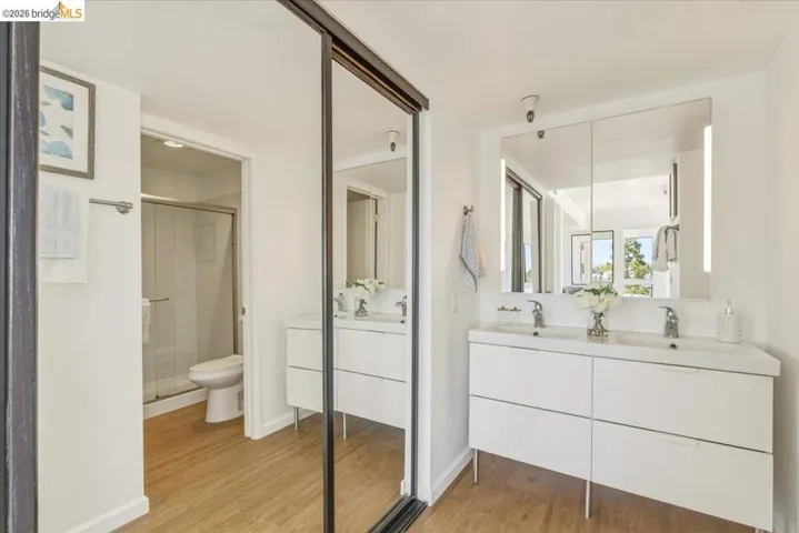 Contemporary bathroom featuring a dual vanity with integrated sinks, illuminated mirrored medicine cabinets, and wood-finish flooring