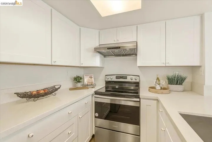 U-shaped kitchen featuring white shaker cabinetry, light-toned countertops, a stainless steel range with matching hood, and an undermount sink