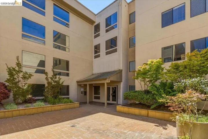 Multi-story building exterior featuring a covered entryway, brick paver courtyard, and integrated landscaping with mature plantings