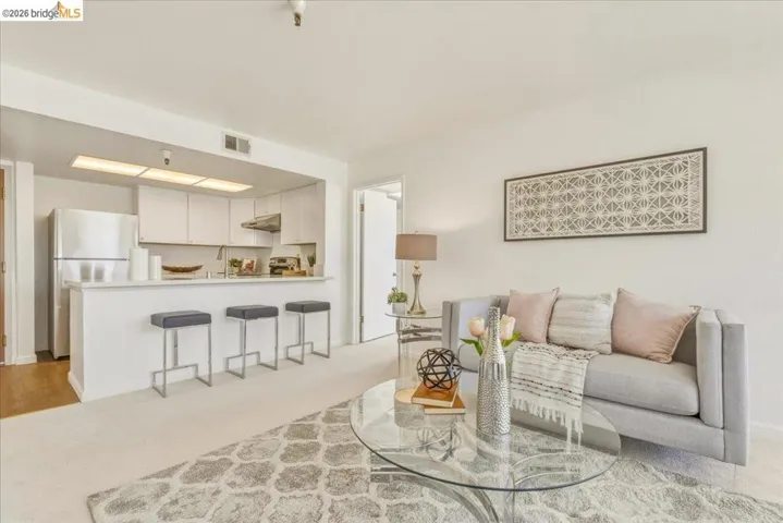 Open-concept living area featuring a kitchen pass-through with breakfast bar seating, white cabinetry, and stainless steel appliances