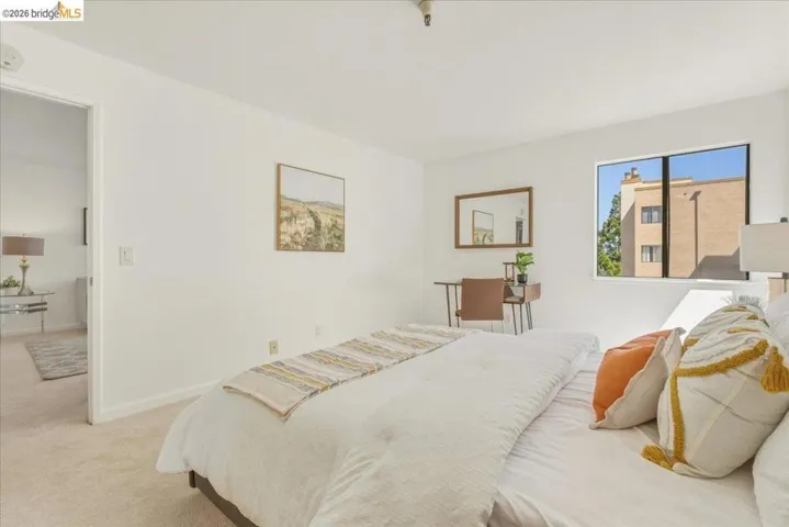 Bright bedroom featuring a large window, plush carpet flooring, white walls, and a convenient doorway opening to an additional room