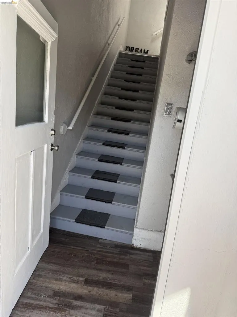 Staircase entry featuring wood-finish flooring, painted treads, and a white handrail