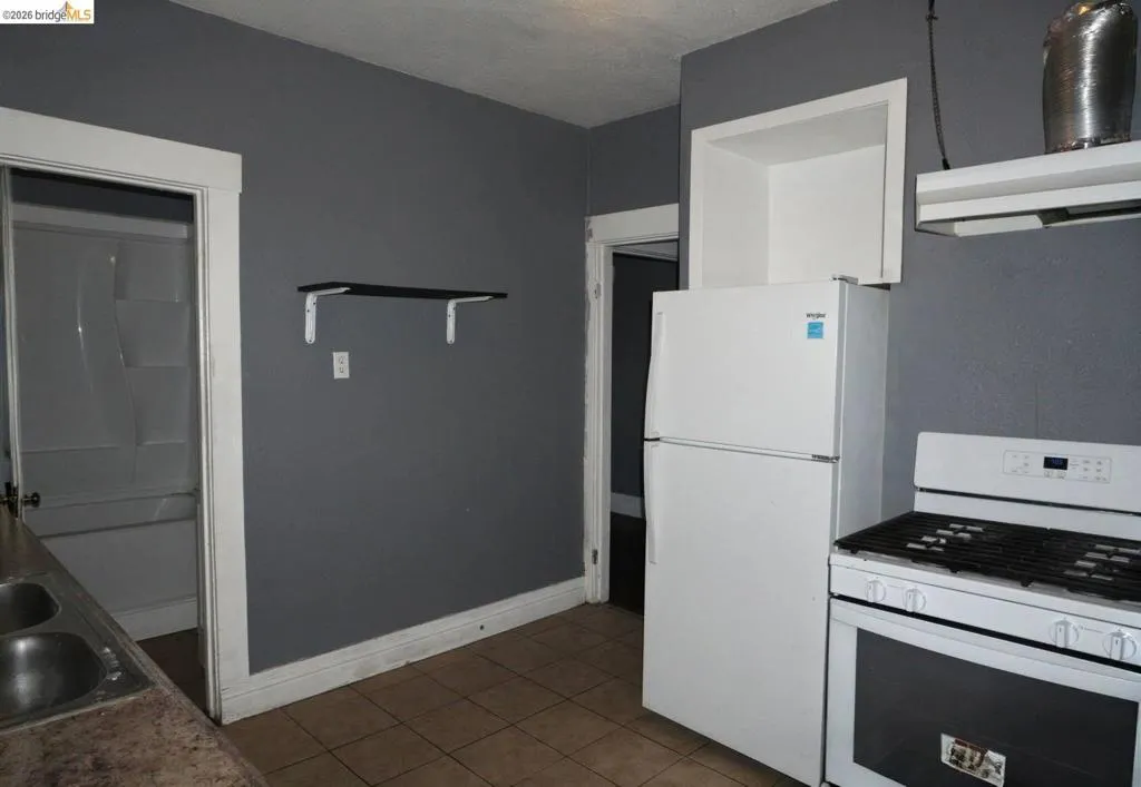 Kitchen area featuring a built-in oven range, white refrigerator, and tiled flooring