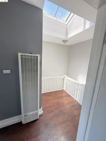 Upper-level landing featuring a prominent skylight, wood-finish flooring, white railing, and a wall-mounted heating unit