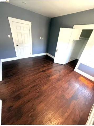 Spacious room featuring wood-finish flooring, dark blue wall paint, white trim, and a white paneled door