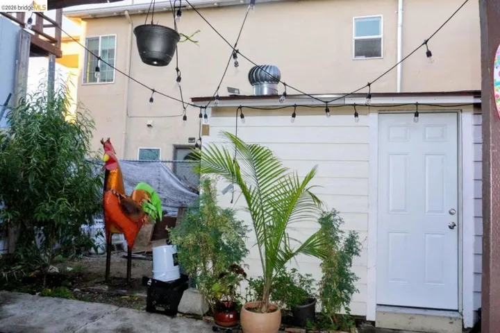 White paneled exterior door with a window unit above, featuring string lighting, potted plants, and concrete paving