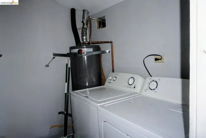 Utility space featuring a water heater with copper piping, a wall-mounted electrical outlet, and white painted walls