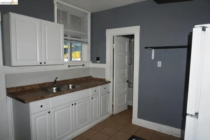Kitchen featuring white cabinetry with dark hardware, a double basin sink, and a brown patterned countertop